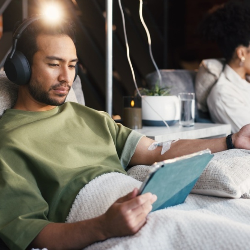 Man receiving IV therapy and looking at a tablet